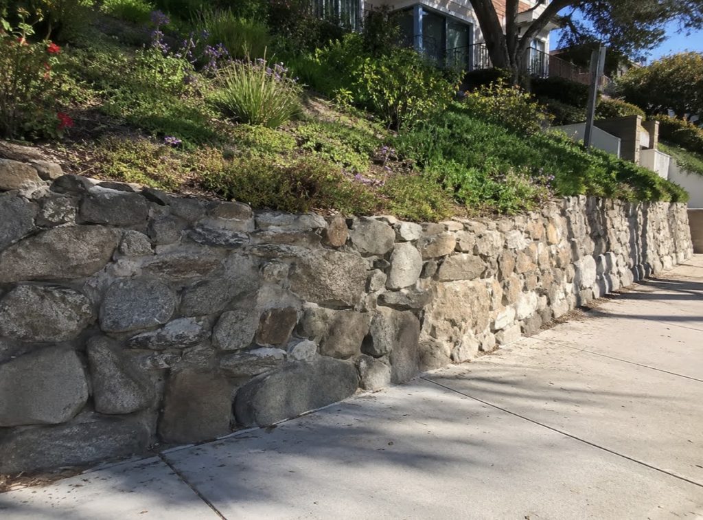 Natural stone retaining wall installation along a Southern California hillside
